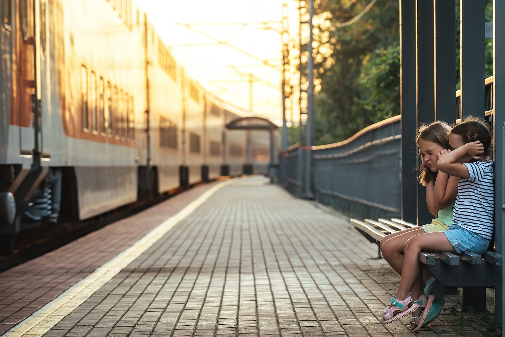 family travel by train, two girls are sitting on a bench at the railway station