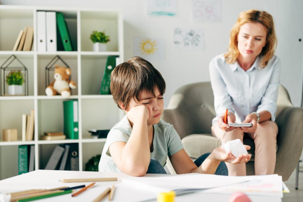 selective focus of kid with dyslexia holding crumpled paper and child psychologist looking at him