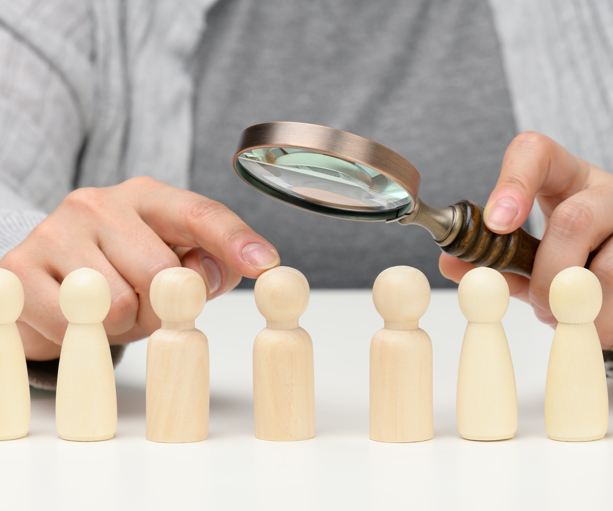 Figurines of men on a white table, a female hand holds a magnifying glass over one