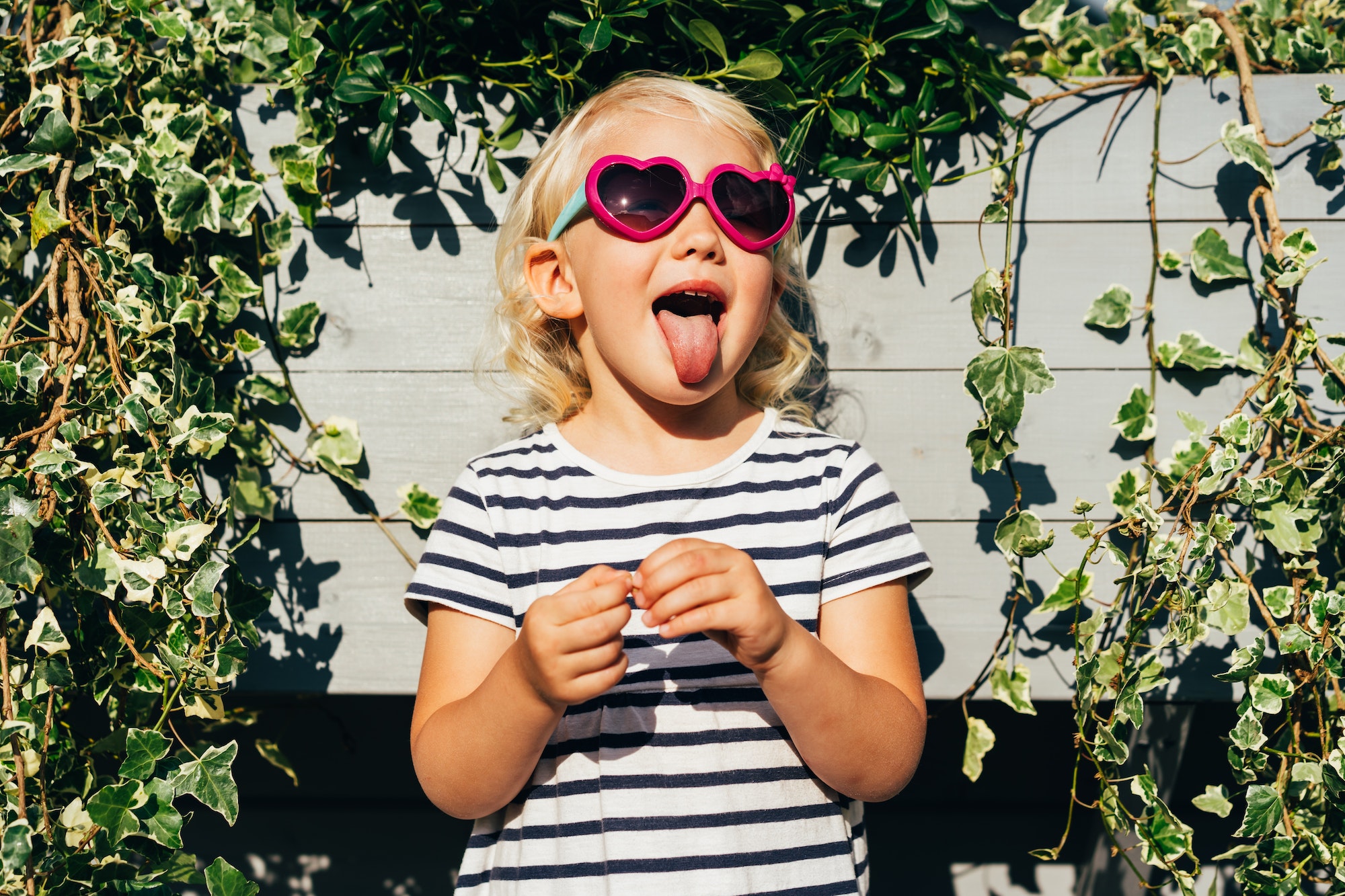 Happy carefree emotional child in summer sunglasses shows tongue and grimaces.