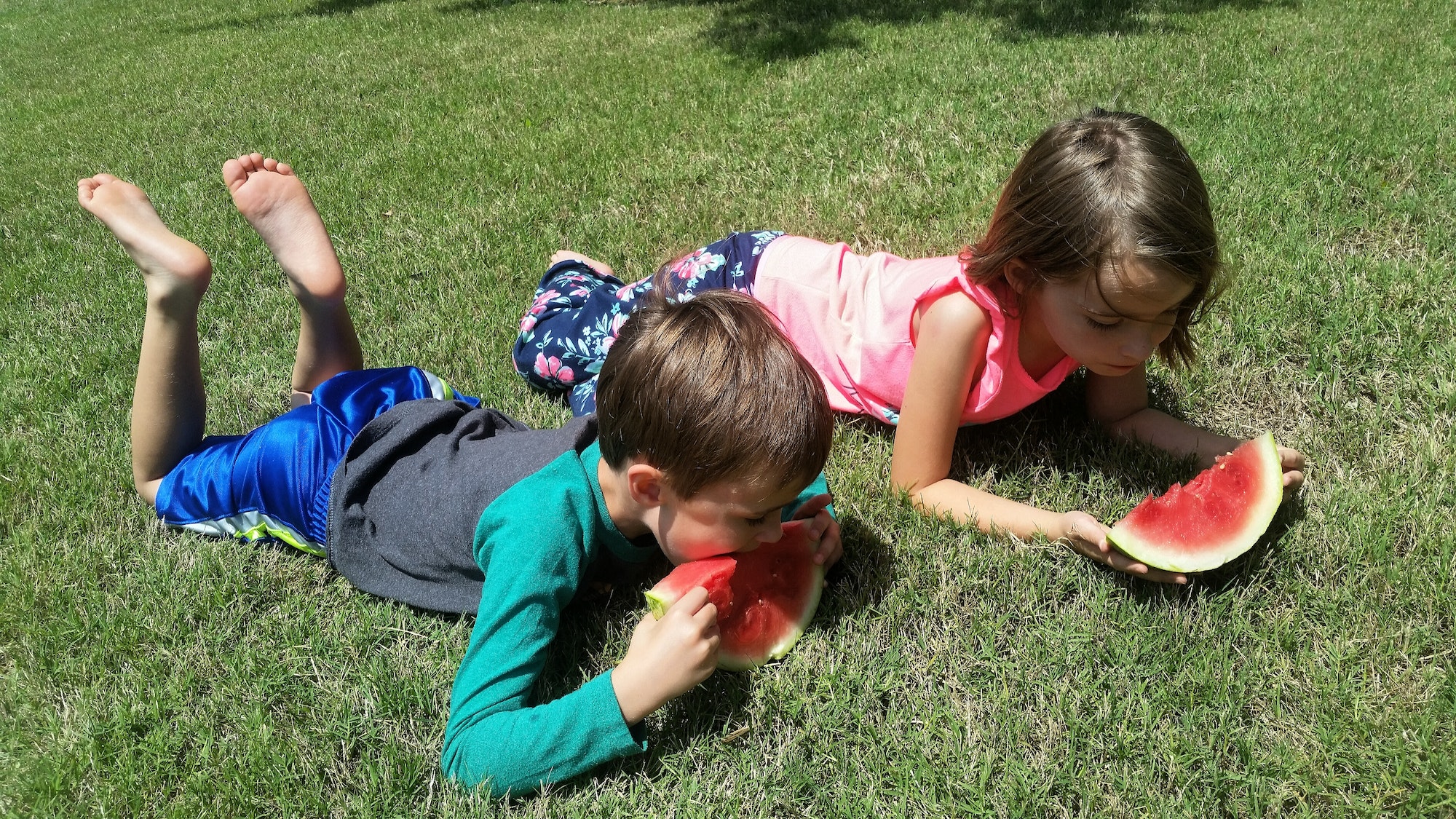 Generation z kids in fron yard staying safe from covid and enjoying a cool refreshing watermelon.