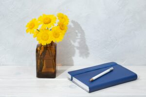 Beautiful flowers in bottle and blue diary on wooden table
