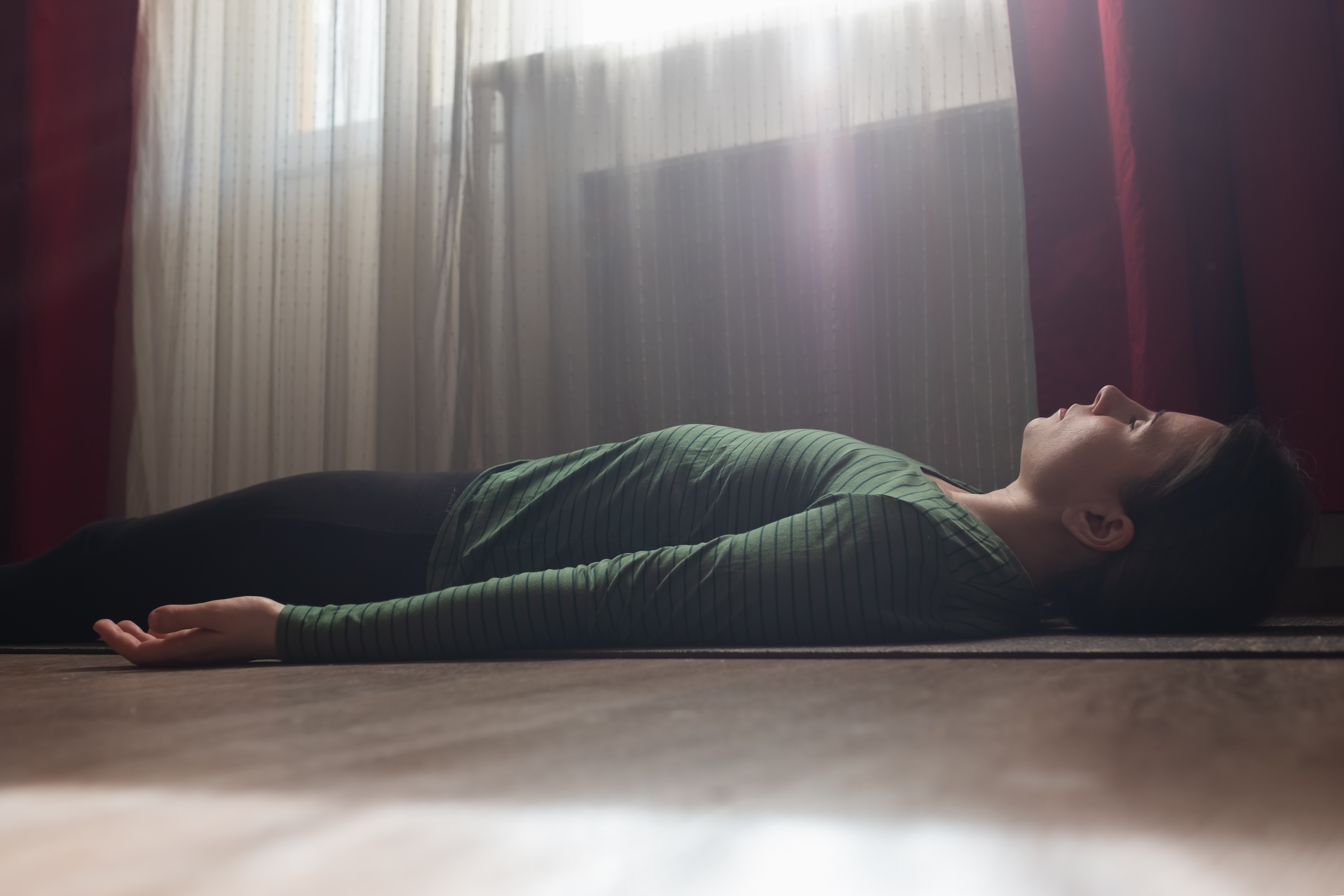 woman rests on the floor of the living room in savasana or corpse pose