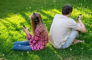 Parents and teens: asitting on the green grass turned away from each other and using mobile phones
